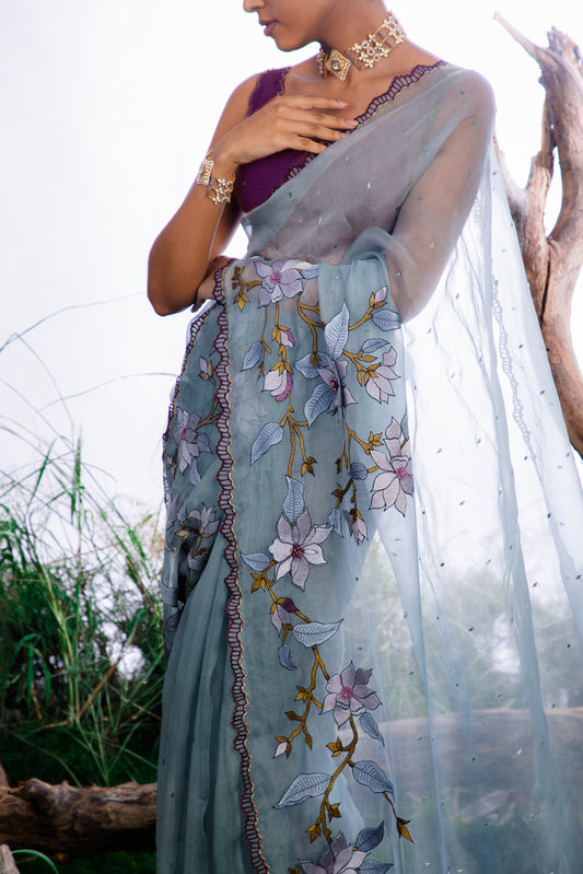 The saree features an enchanting display of 3D embroidered floral motifs that cascade like a blooming vine across the fabric.