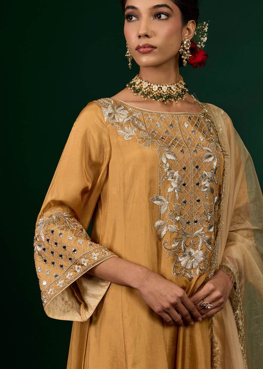 Woman wearing a mustard yellow embroidered outfit with a green background