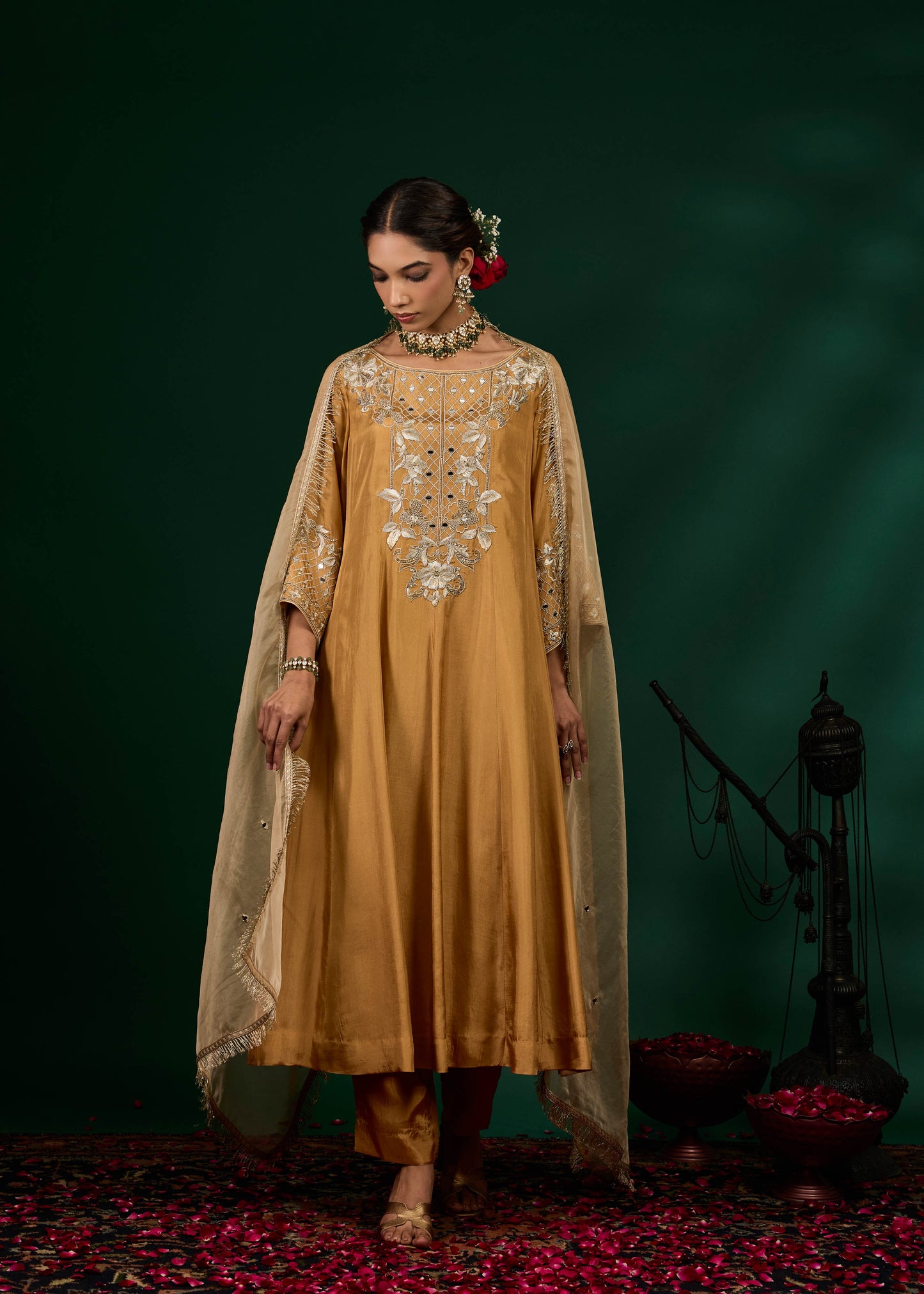 Woman wearing a mustard yellow traditional outfit with intricate embroidery against a dark background.
