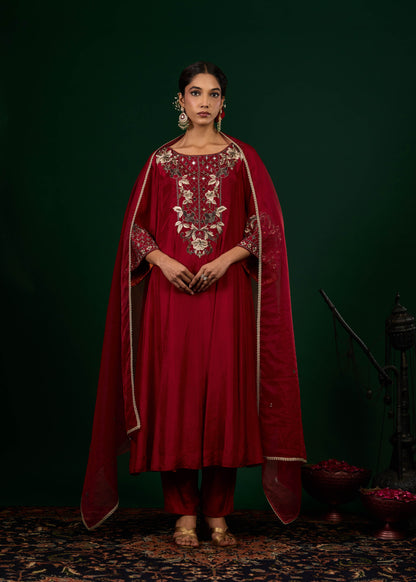 Woman wearing a red traditional outfit with intricate embroidery against a dark green background