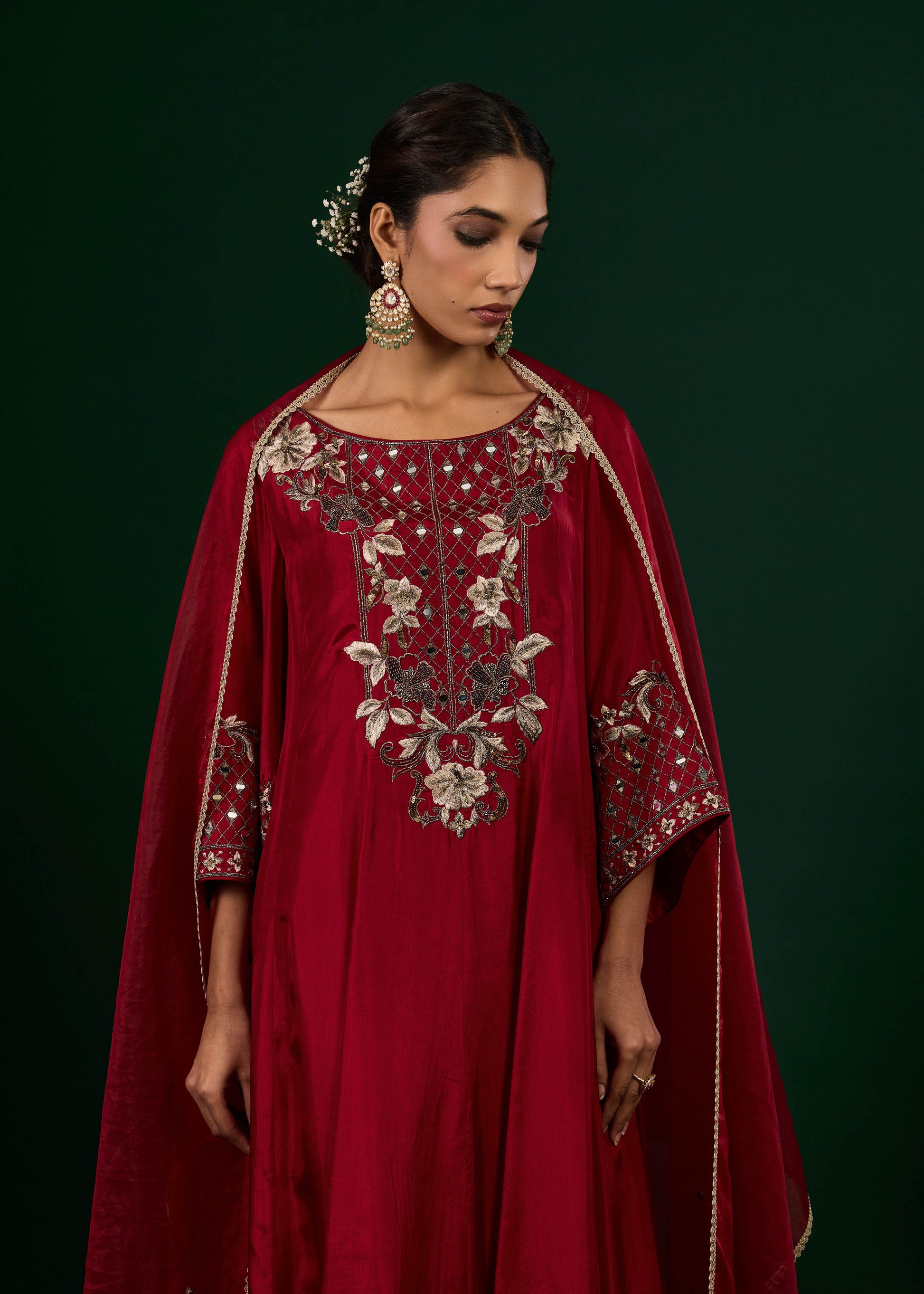 Woman wearing a red embroidered dress with a cape against a dark background