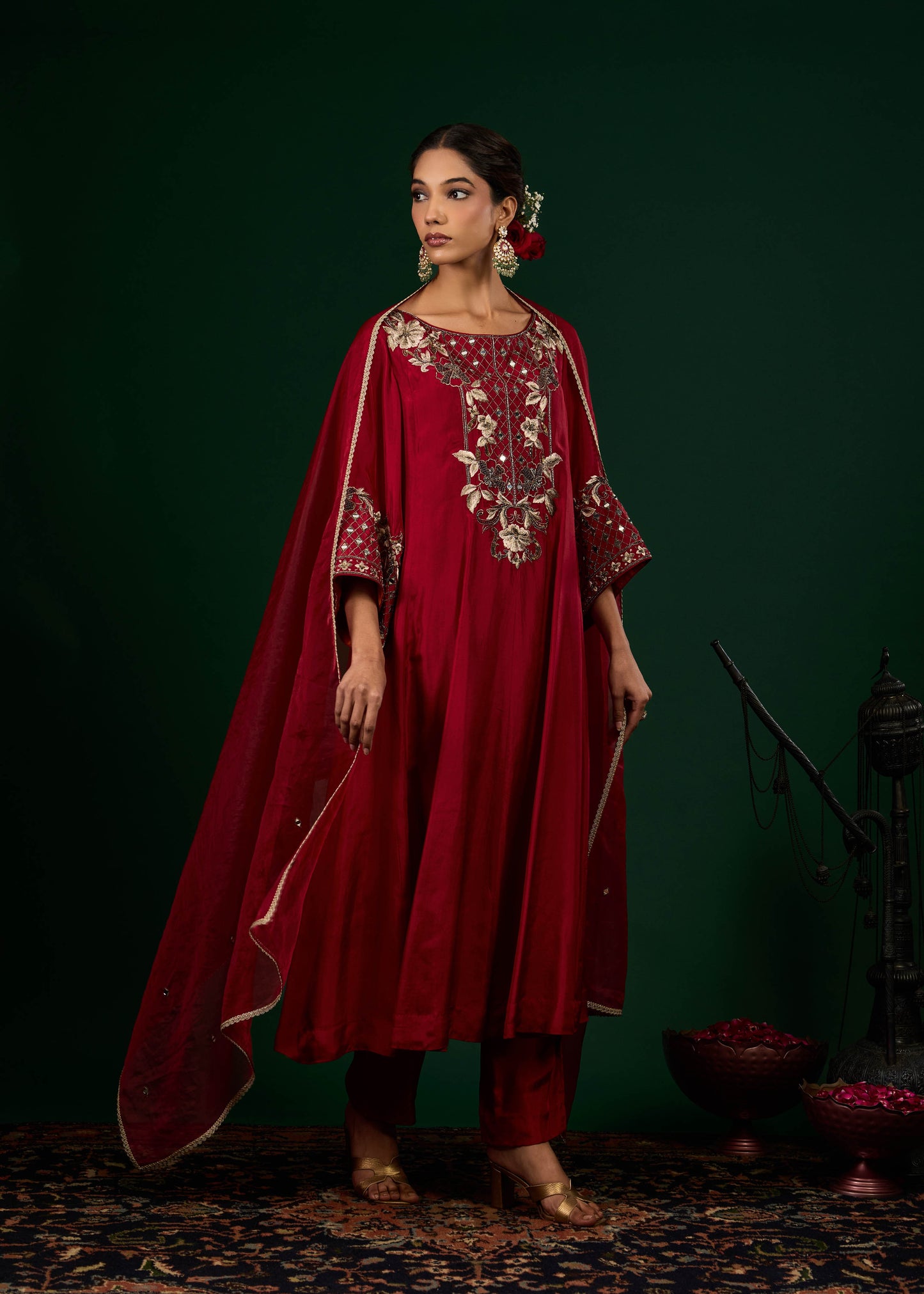 Woman wearing a red traditional outfit with intricate embroidery against a dark green background