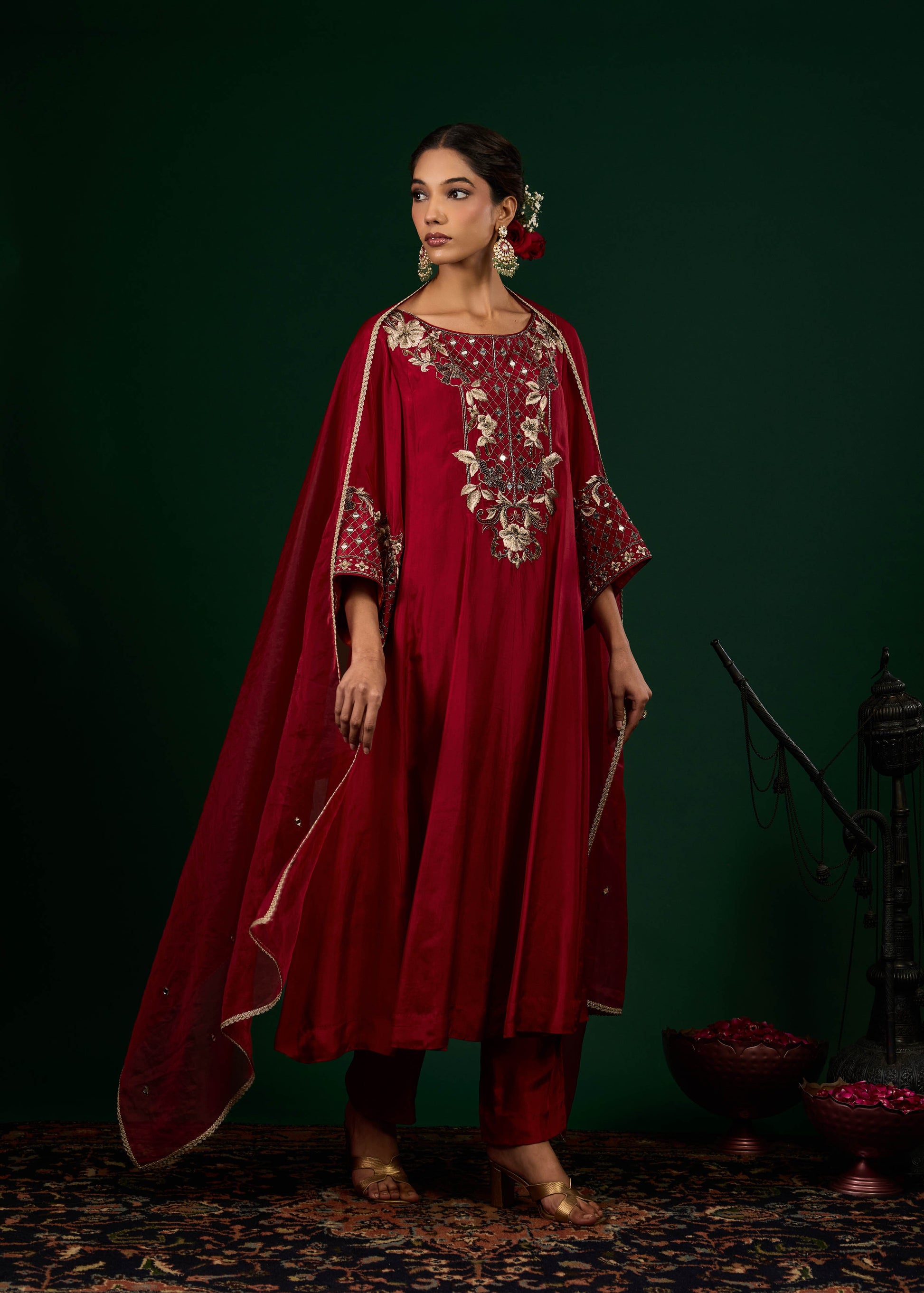 Woman wearing a red traditional outfit with intricate embroidery against a dark green background