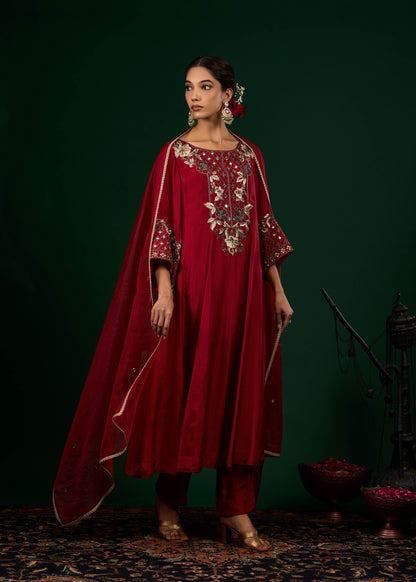 Woman wearing a red traditional outfit with intricate embroidery against a dark green background